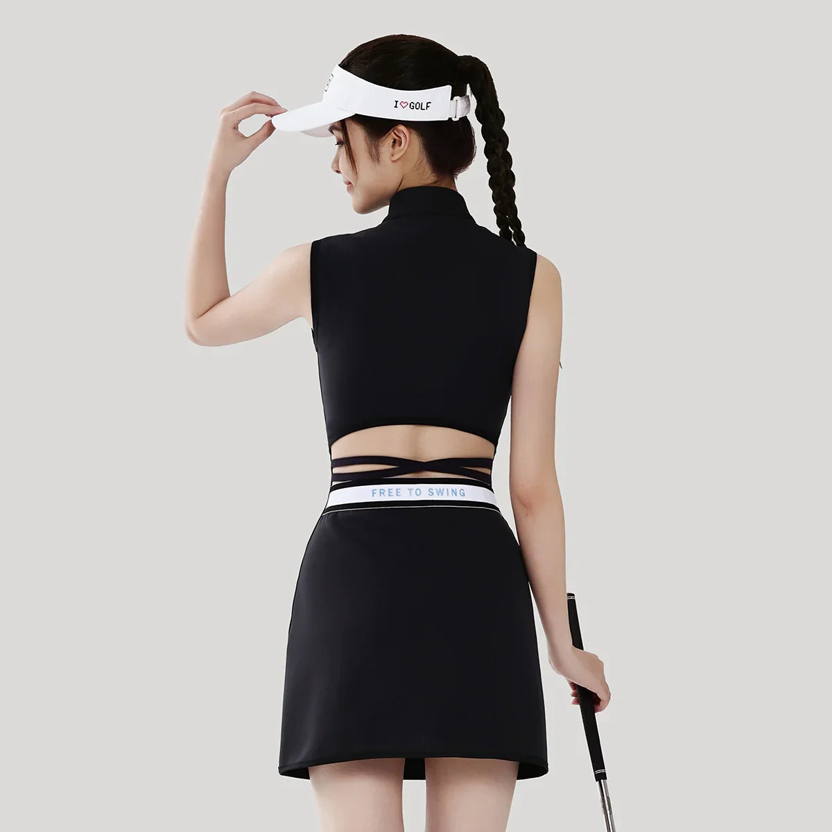 Woman in black athletic wear with a visor, holding a golf club on a light gray background