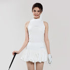 Woman wearing a white tennis outfit with a racket on a plain background