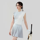 Woman in light gray sleeveless top and pleated skirt holding a golf club on a plain background