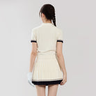 Woman wearing a cream-colored dress with black trim on a plain background